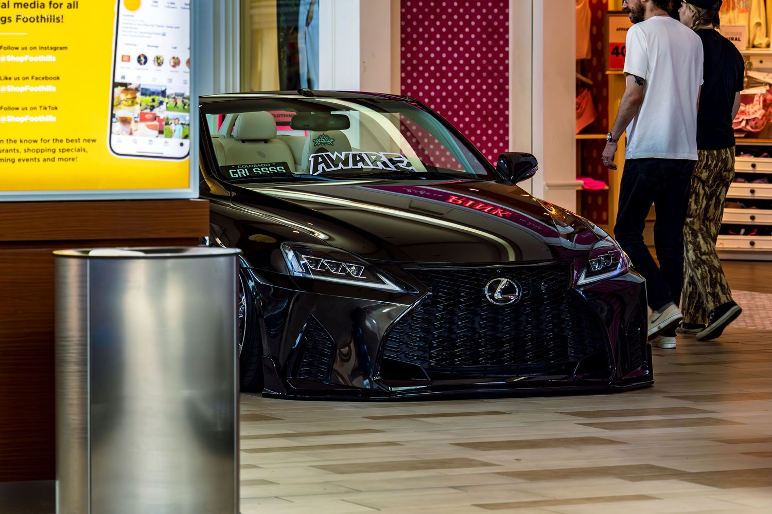 Murdered out black Lexus LC with AWARE banner displayed inside shopping mall at custom car show.