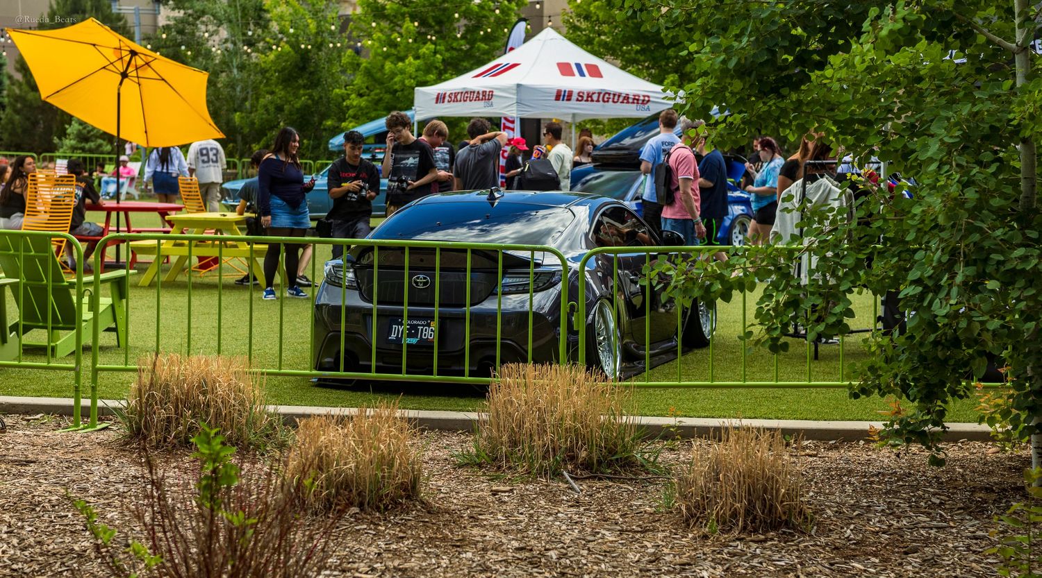 A sleek sports car displayed at an outdoor car show with colorful tents and spectators in the background.