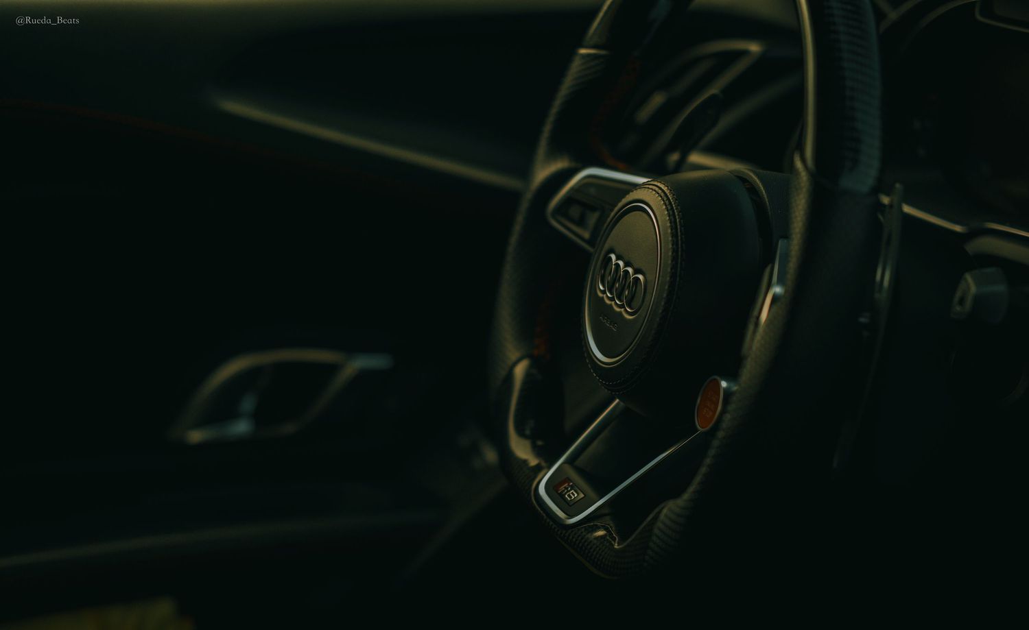 Dark Audi cockpit with illuminated flat-bottom steering wheel detail.