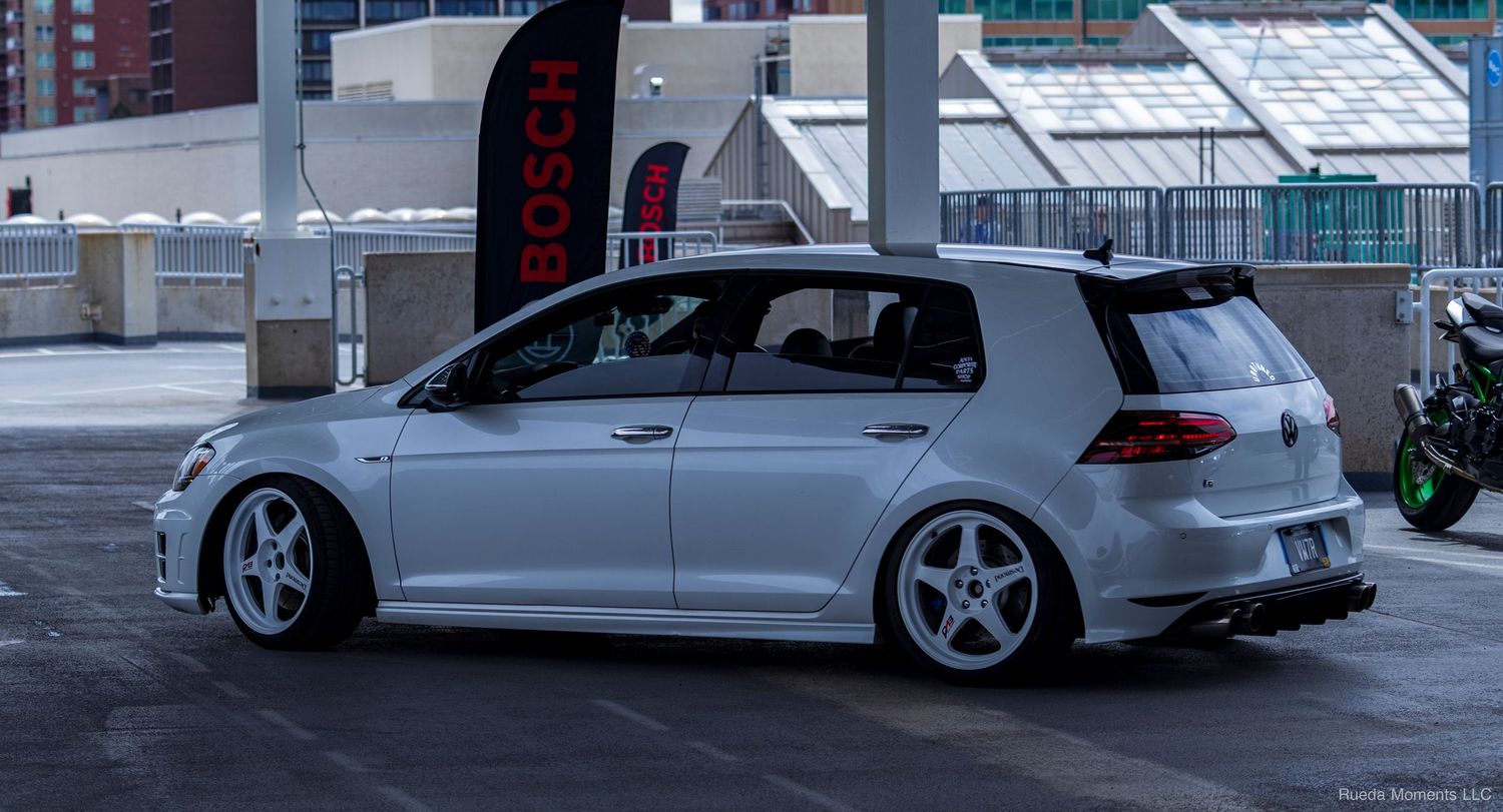 White VW Golf GTI lowered on white wheels at an outdoor car show.