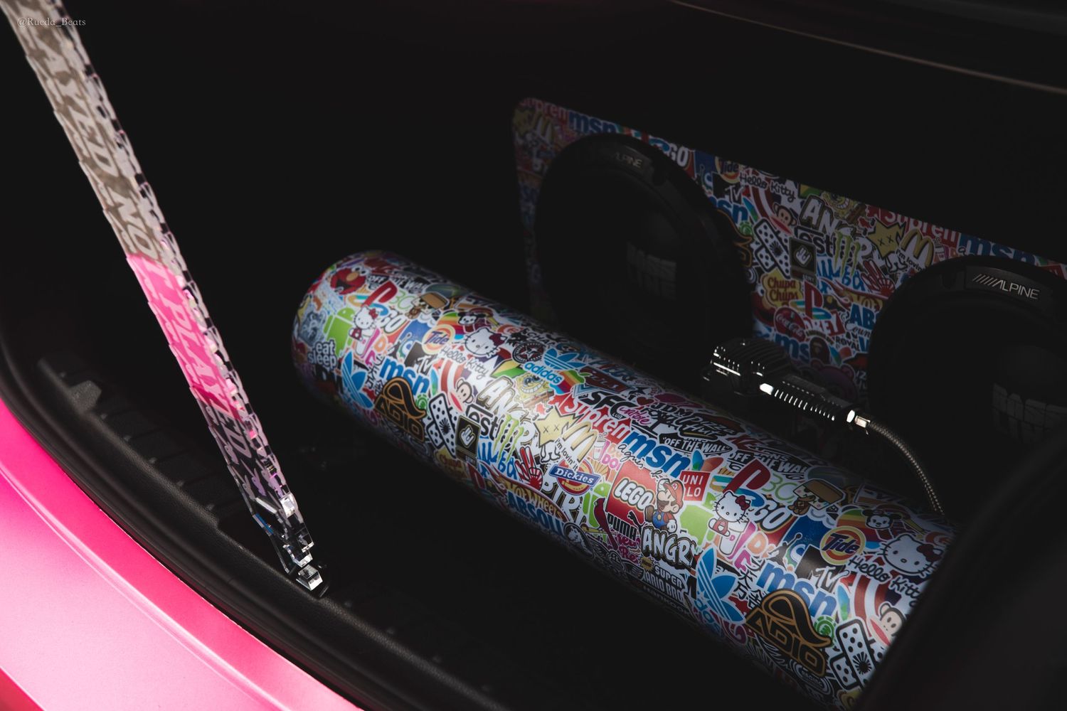 Sticker bomb wrapped subwoofer and audio equipment inside a pink car trunk.