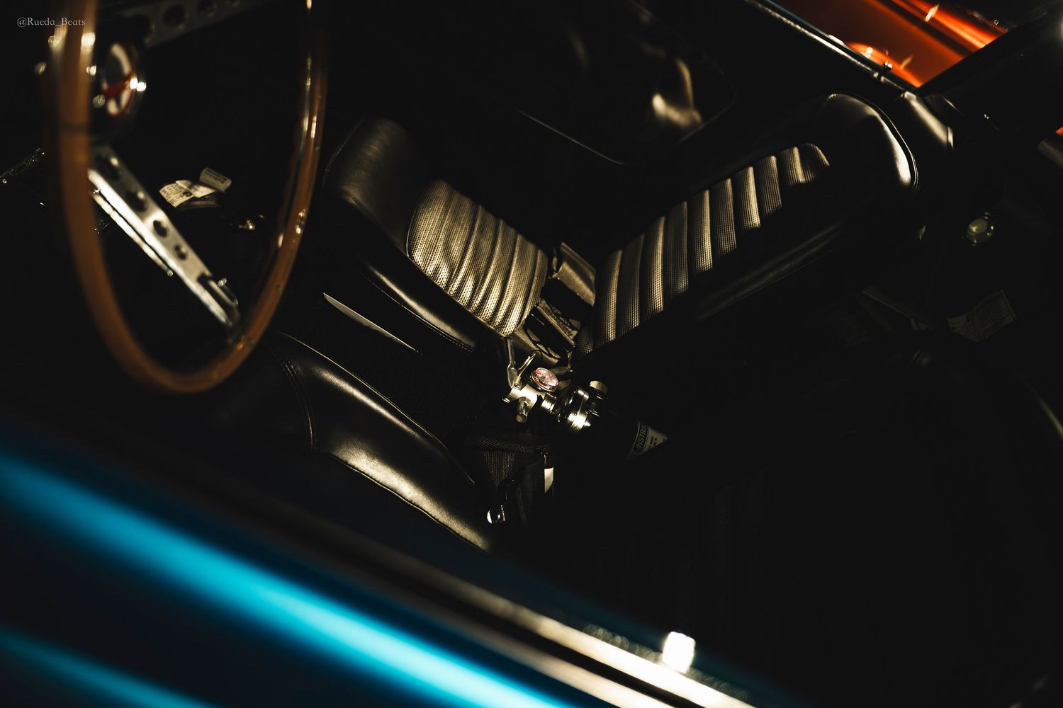 Close-up of a classic car engine bay showing dark metal components with blue bodywork in dim lighting.