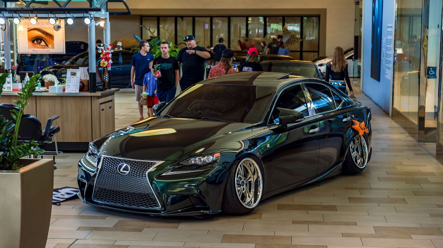 Dark green Lexus IS bagged and stanced on custom wheels at a mall car show.
