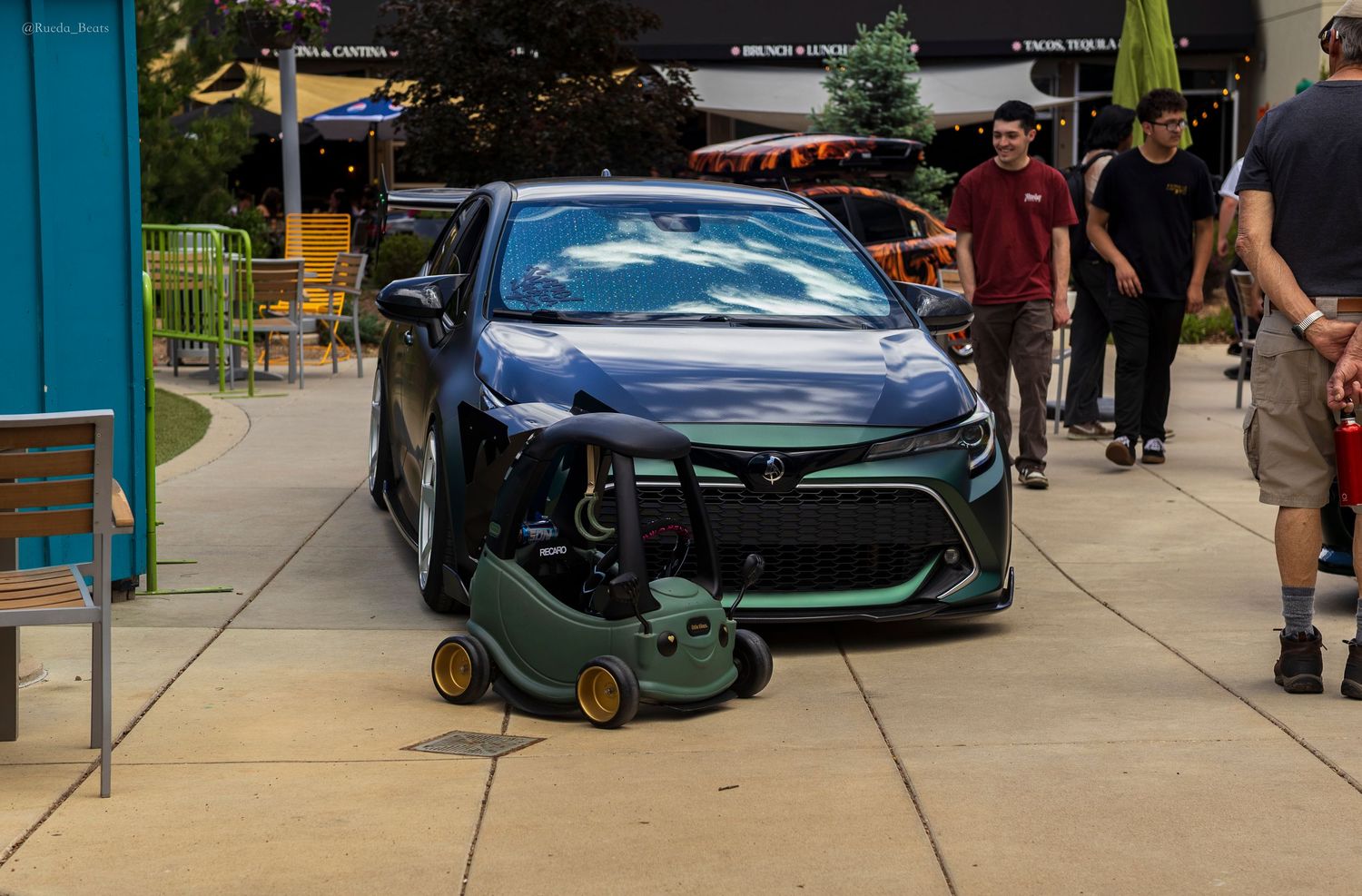Modified dark blue Toyota Corolla with wide body kit parked next to toy lawn mower.