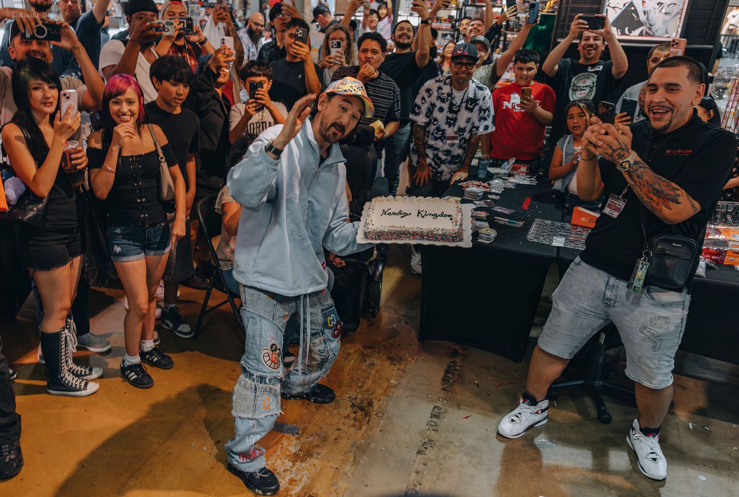 Man holding a birthday cake surrounded by cheering fans at an indoor event.