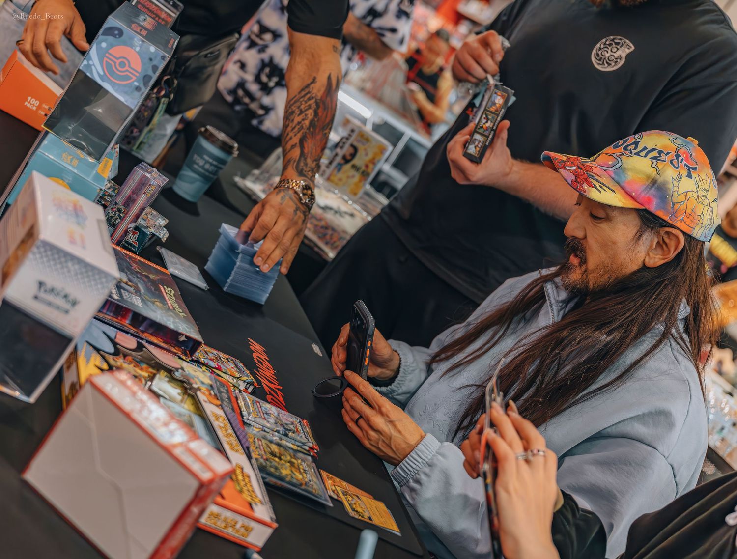 Man in colorful cap examining trading cards at a busy collectibles store counter.
