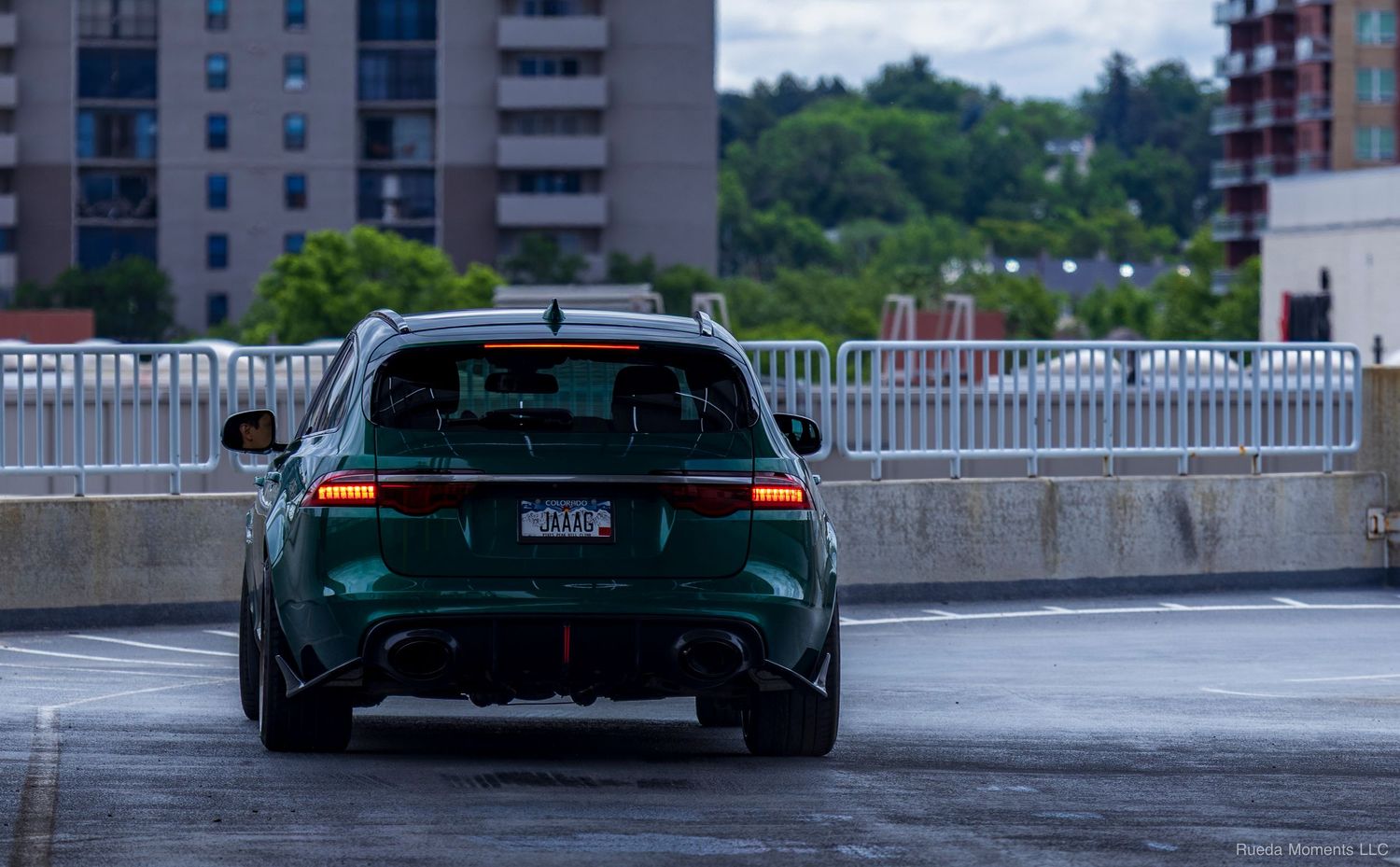 A dark green Audi RS6 Avant wagon drives away on a wet urban parking structure road.
