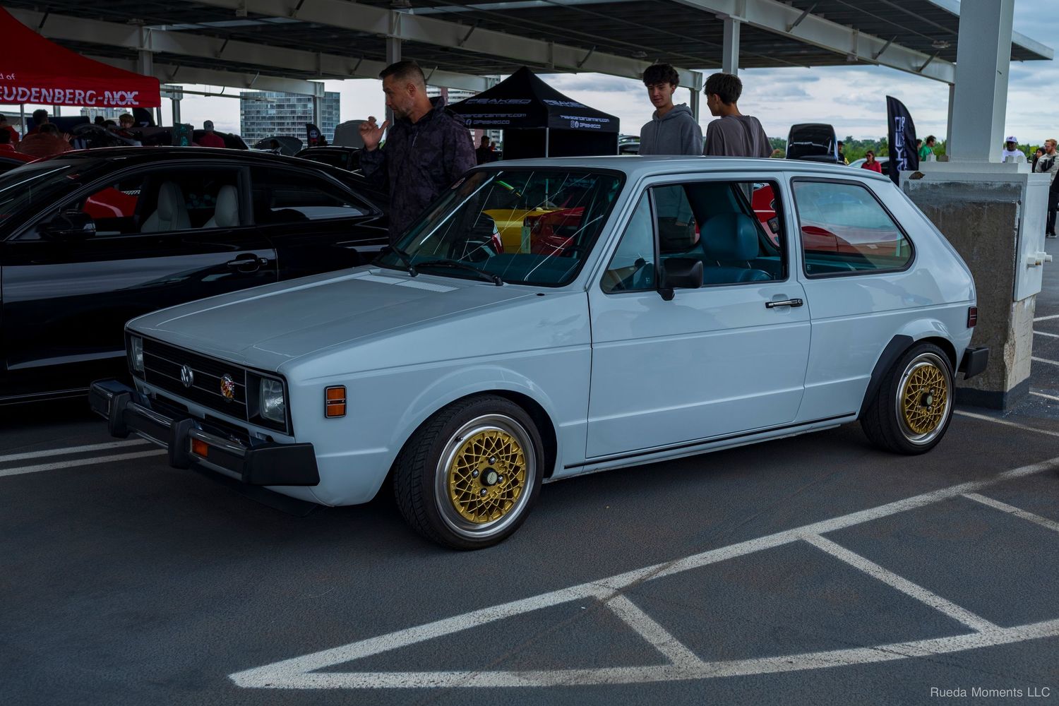 White Volkswagen Golf Mk1 with gold BBS wheels at an outdoor car show.