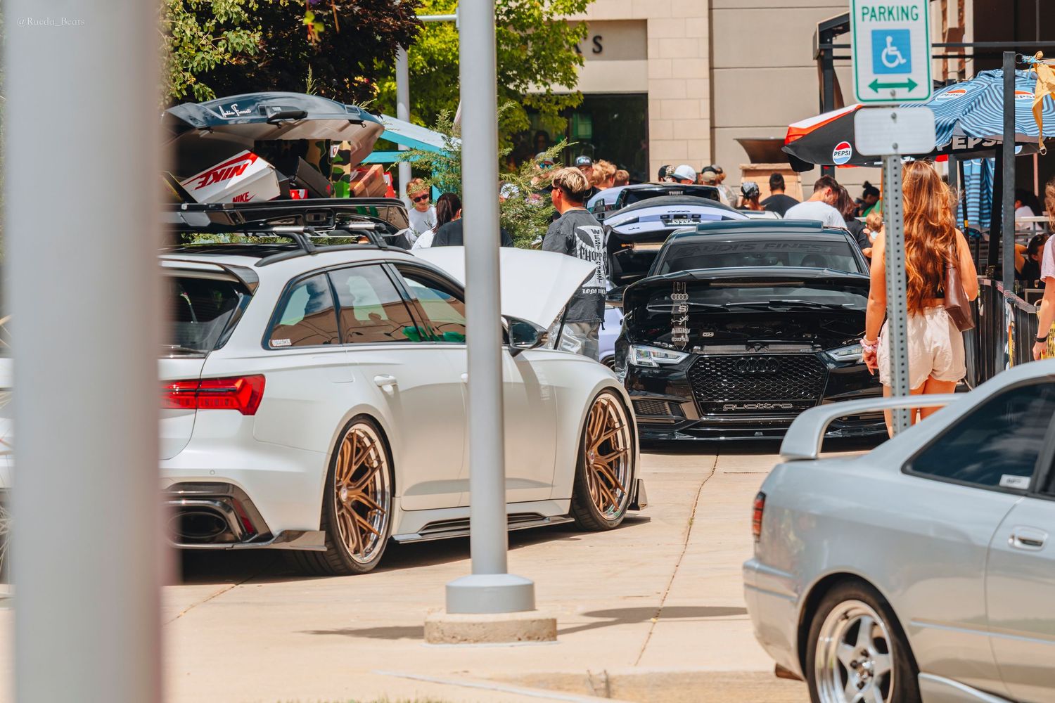 Modified white Audi RS6 wagon with roof rack parked at outdoor car show.