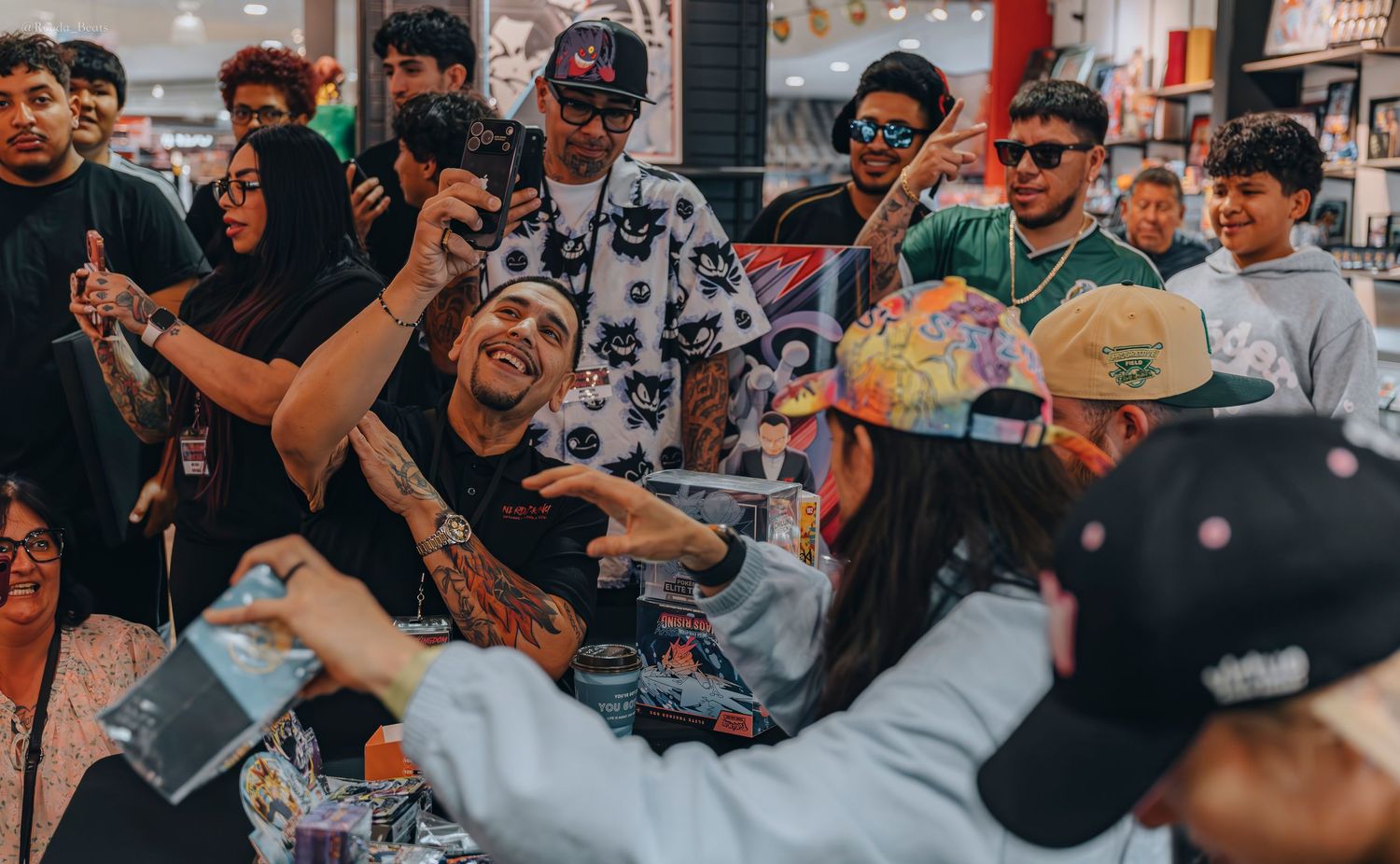 Tattooed man taking selfies with excited fans at a crowded retail store signing event.