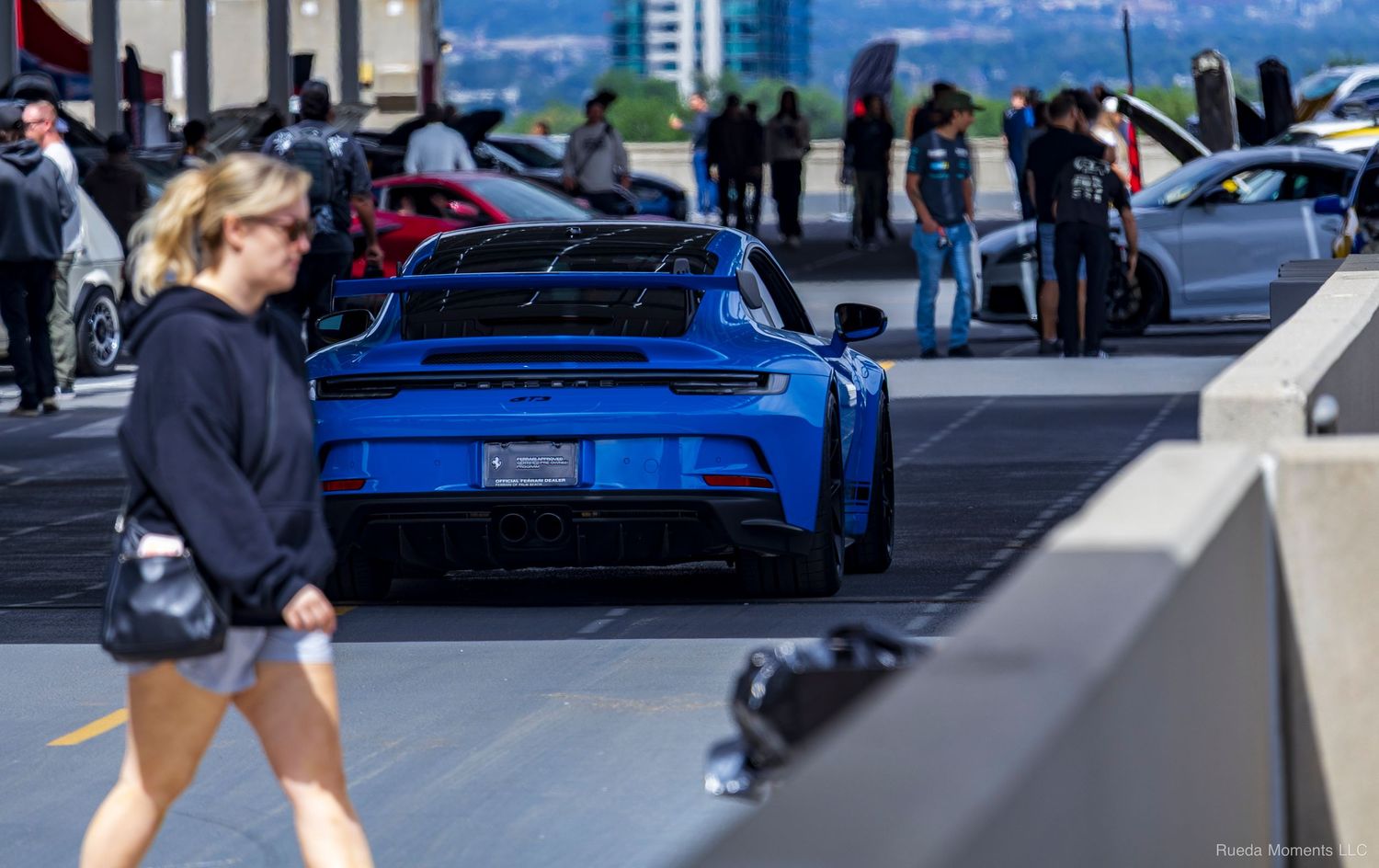 Blue Porsche 911 GT3 at a car meet with a woman walking past in the foreground.