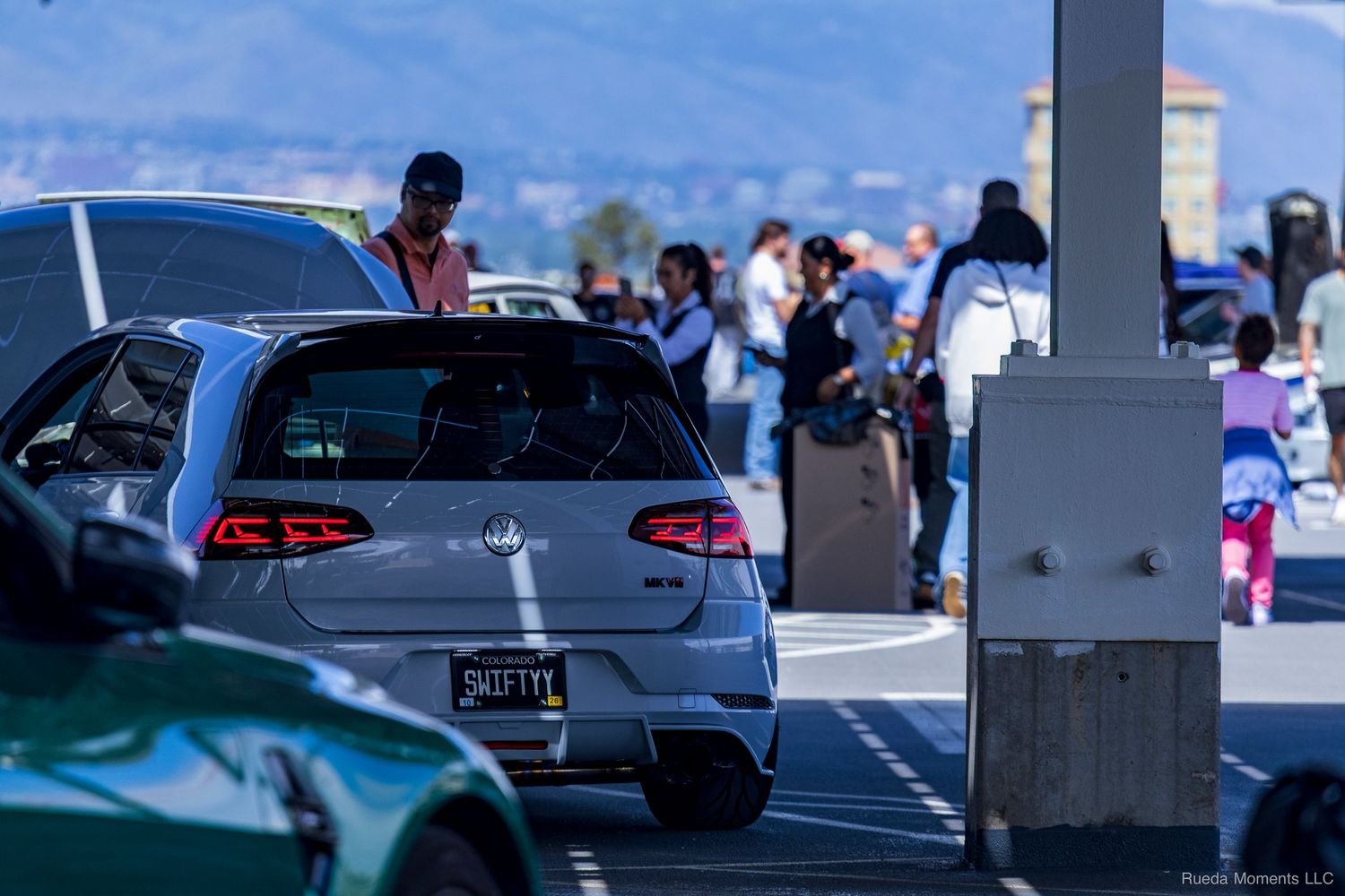 White VW Golf GTI at a car meet with spectators in the background on a sunny day.