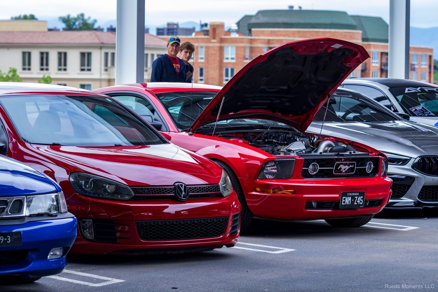 Red Volkswagen GTI and Ford Mustang with hood open displayed at outdoor car show.