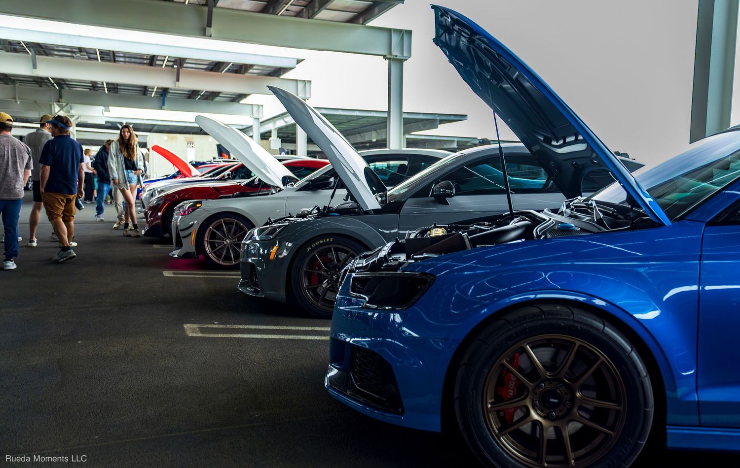 Row of performance cars with hoods open on display at a covered outdoor car show event.