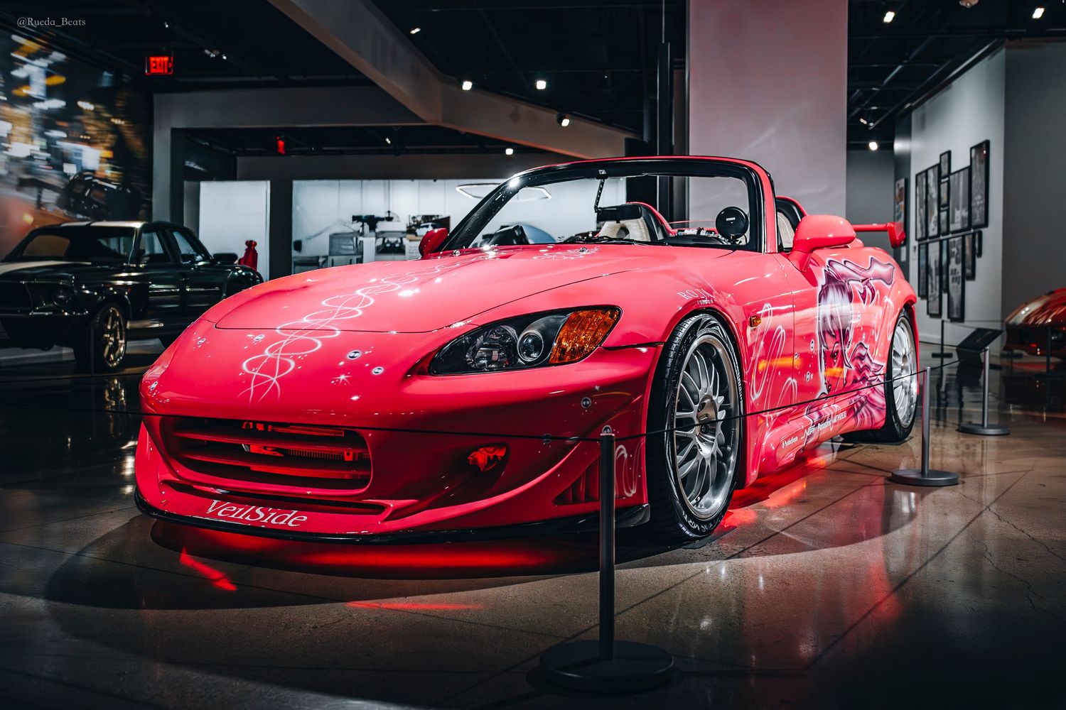 Red Honda S2000 convertible with custom white floral graphics on display at car museum exhibit.