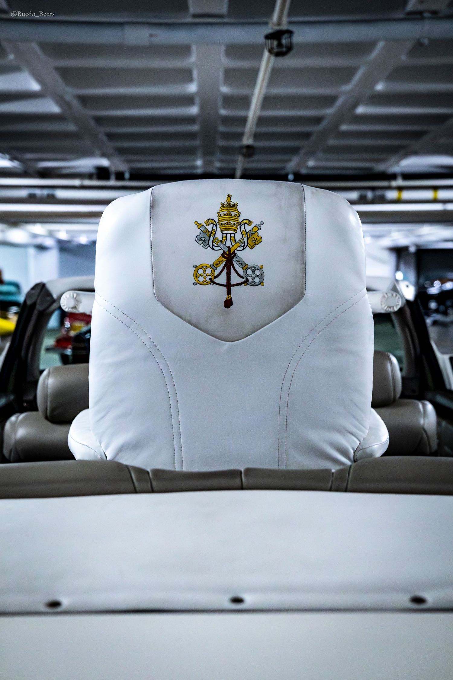 White leather car headrest embroidered with the Vatican papal coat of arms symbol.