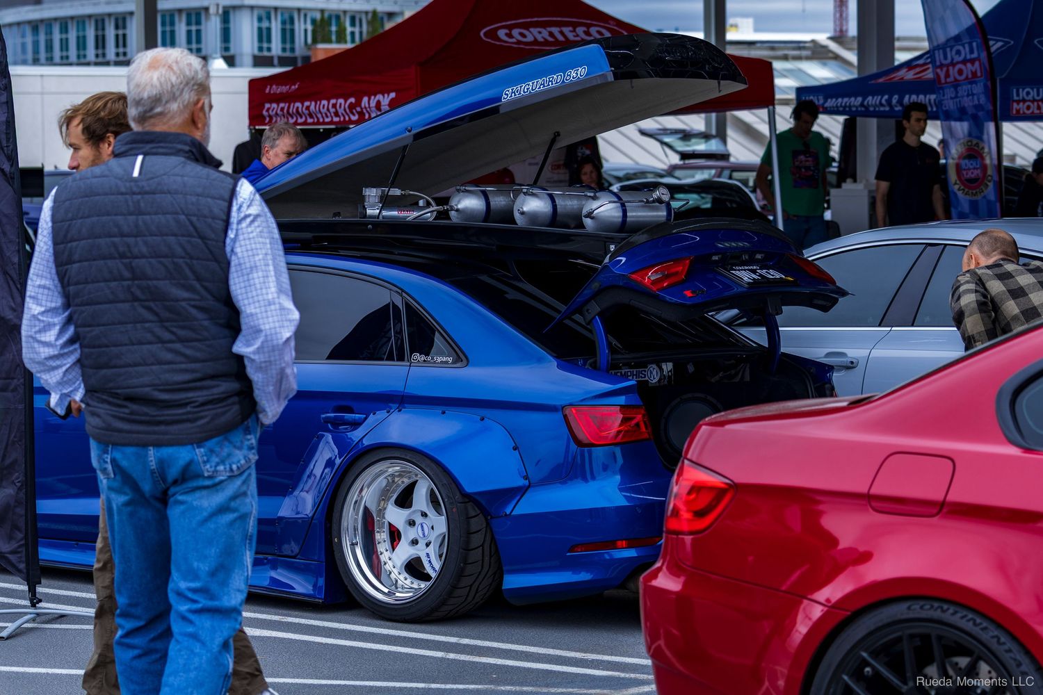 Modified blue Audi S3 on air suspension with open trunk at a car show.