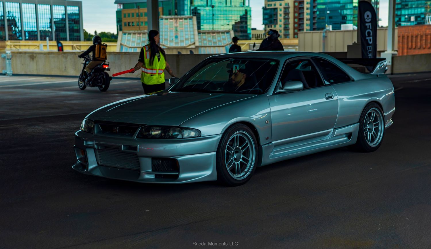 Silver Nissan Skyline R33 GT-R with wide body kit parked at an urban car meet.