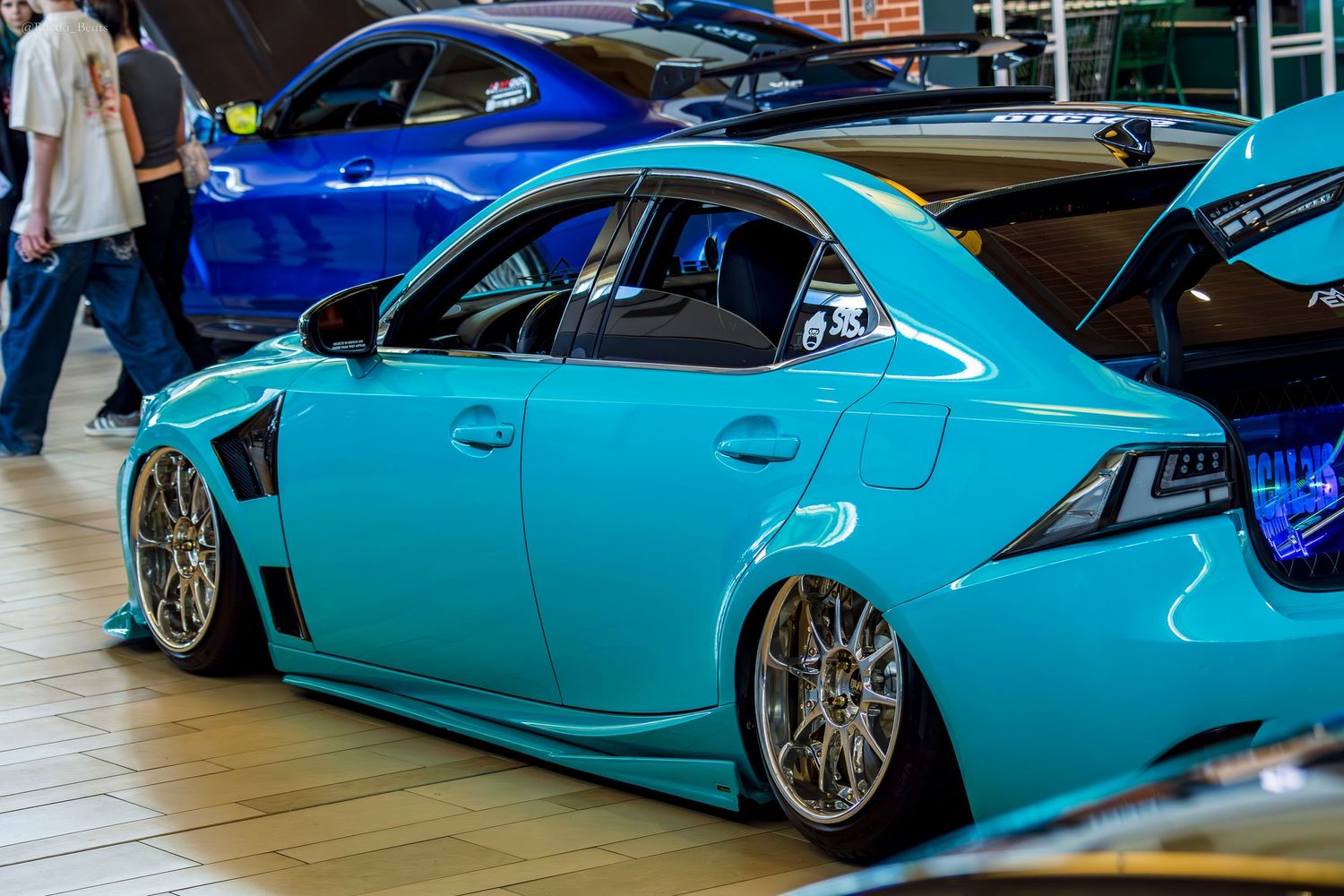 Tiffany blue stanced Mitsubishi Lancer Evo on chrome wheels at an indoor car show.