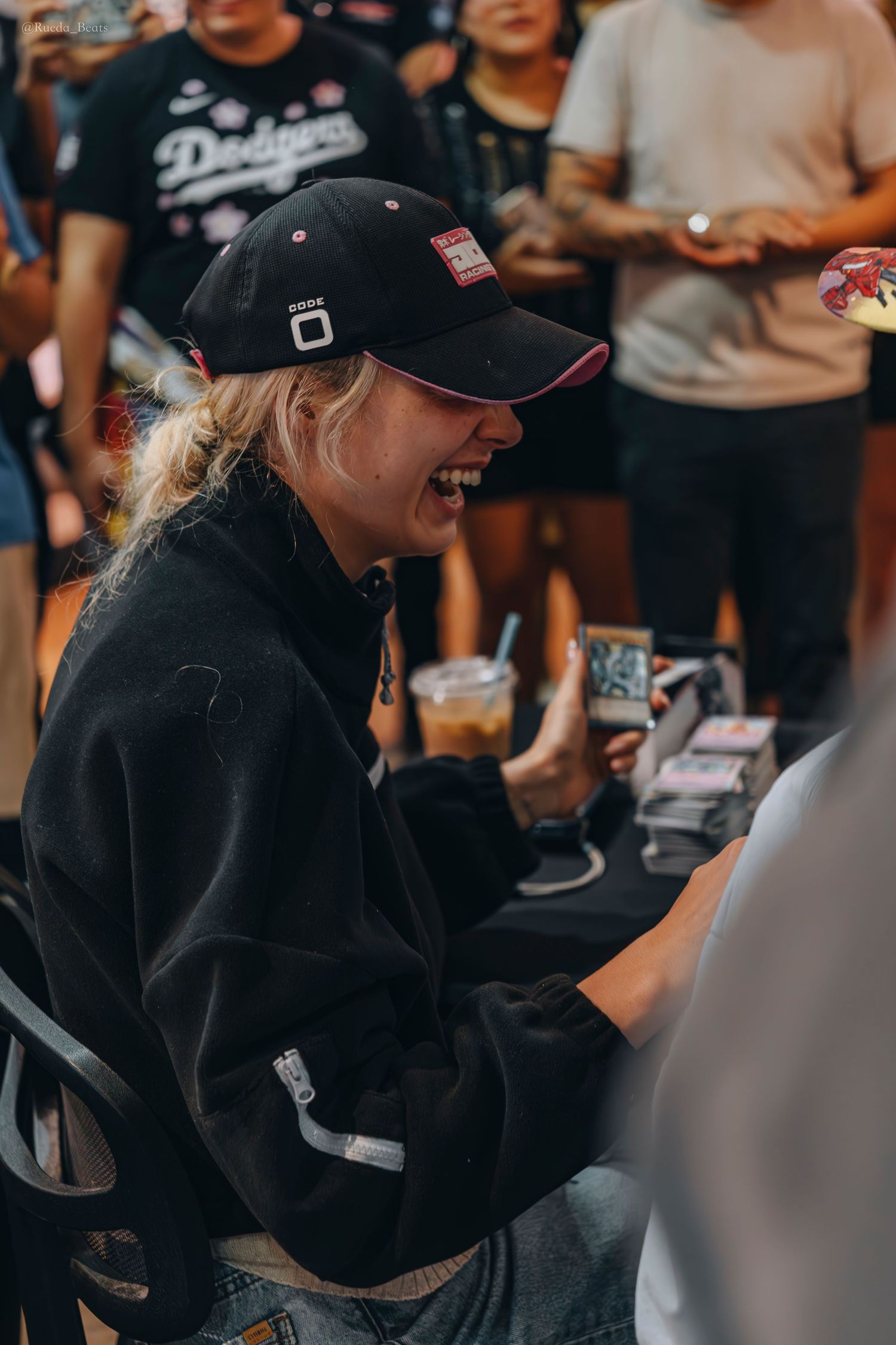Smiling blonde woman in black cap enjoys trading card event.