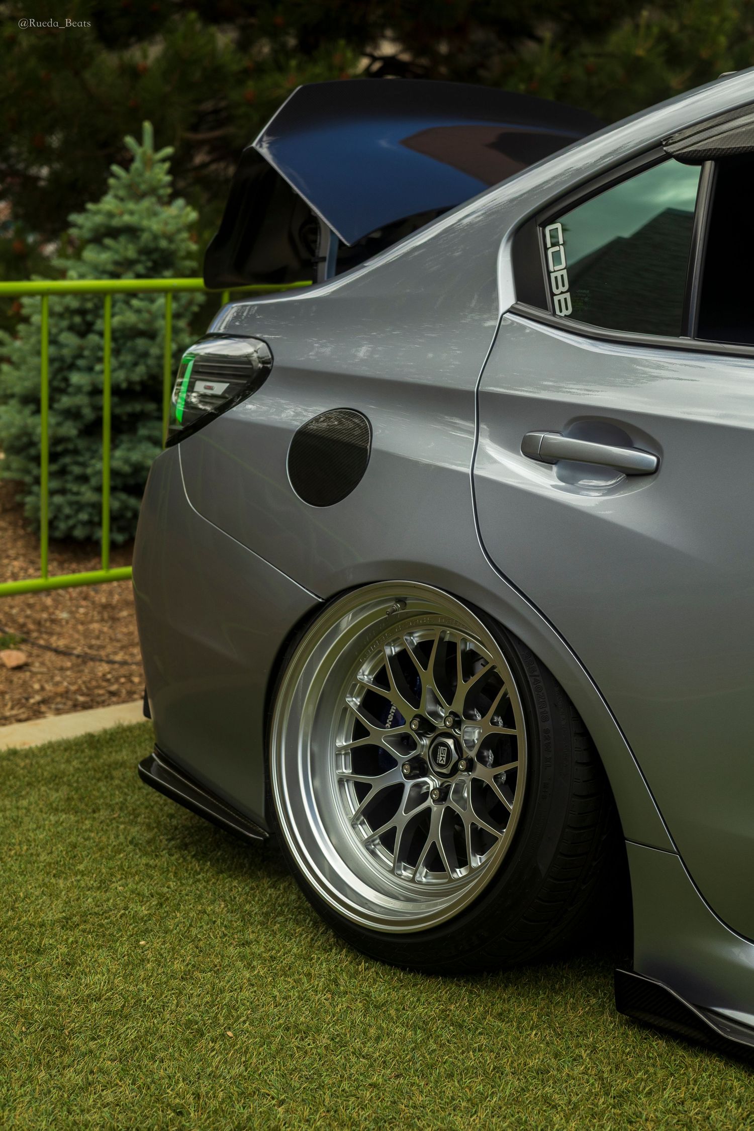 Close-up of a lowered grey Subaru with deep-dish BBS wheels and COBB sticker at a car show.
