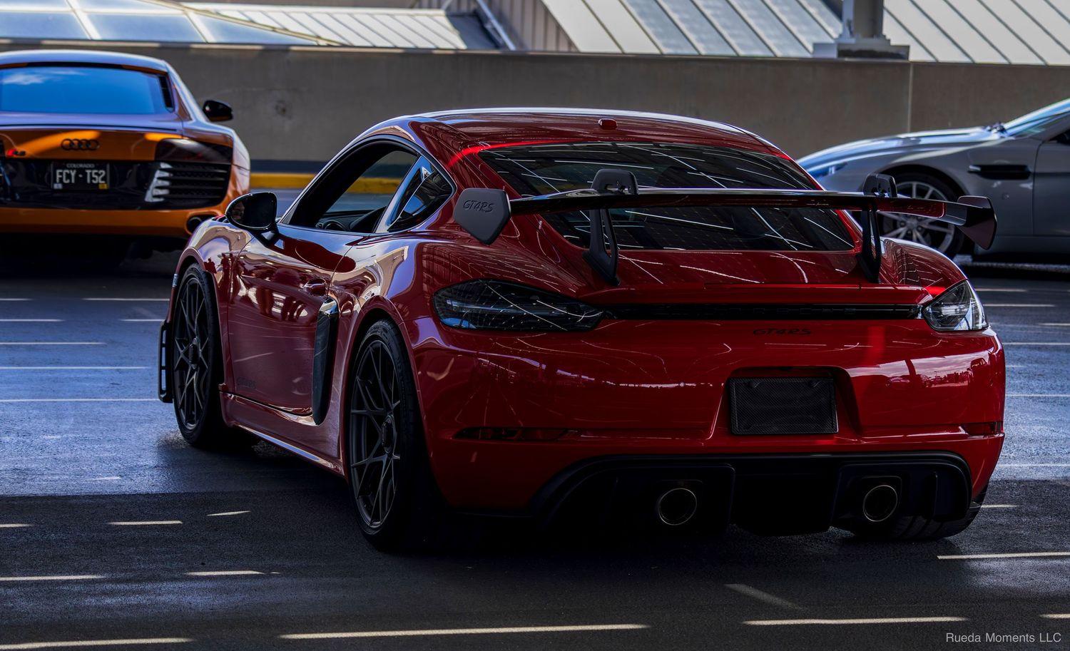 Red Porsche 718 Cayman GT4 rear view with carbon fiber spoiler in a parking garage.