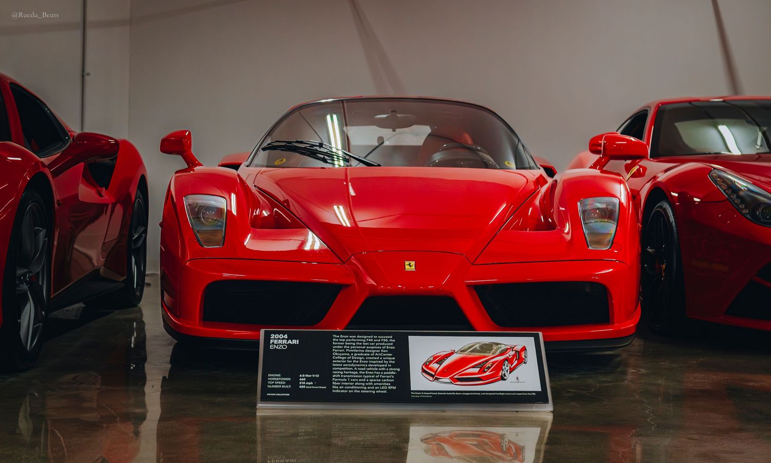 Front view of a red Ferrari Enzo on museum display with artwork placard below.