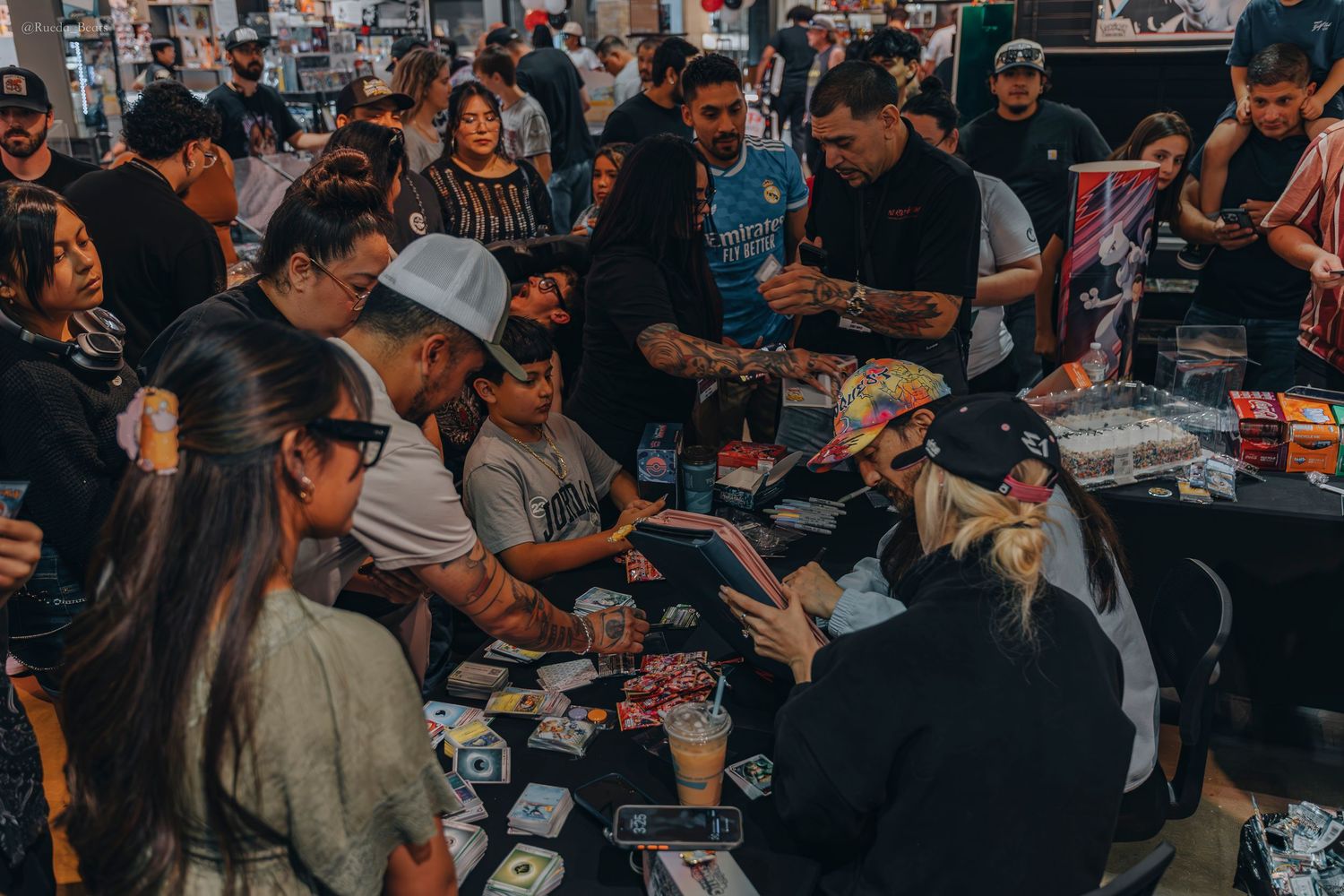 Diverse crowd of fans gathered around a table at a trading card signing event.