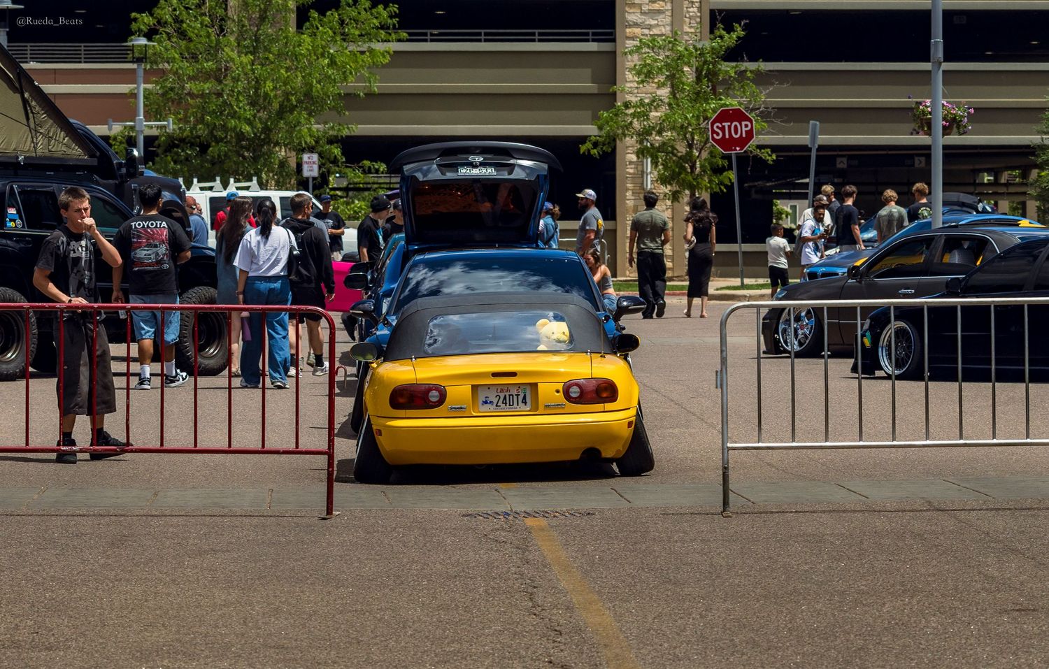 Yellow Mazda Miata with open trunk on display at an outdoor car show event.