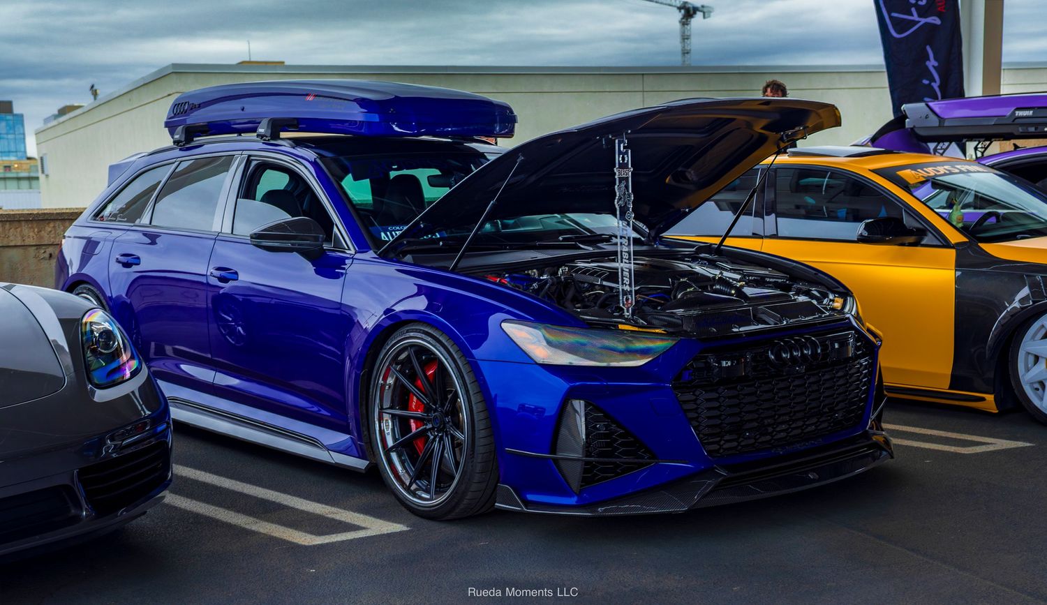 Blue Audi RS6 wagon with carbon hood and roof box at car show.