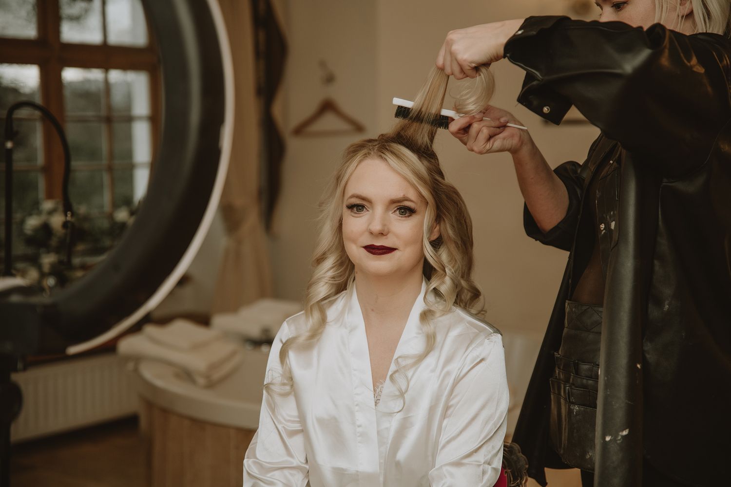 Bride in white robe gets hair styled with curling iron before wedding ceremony.