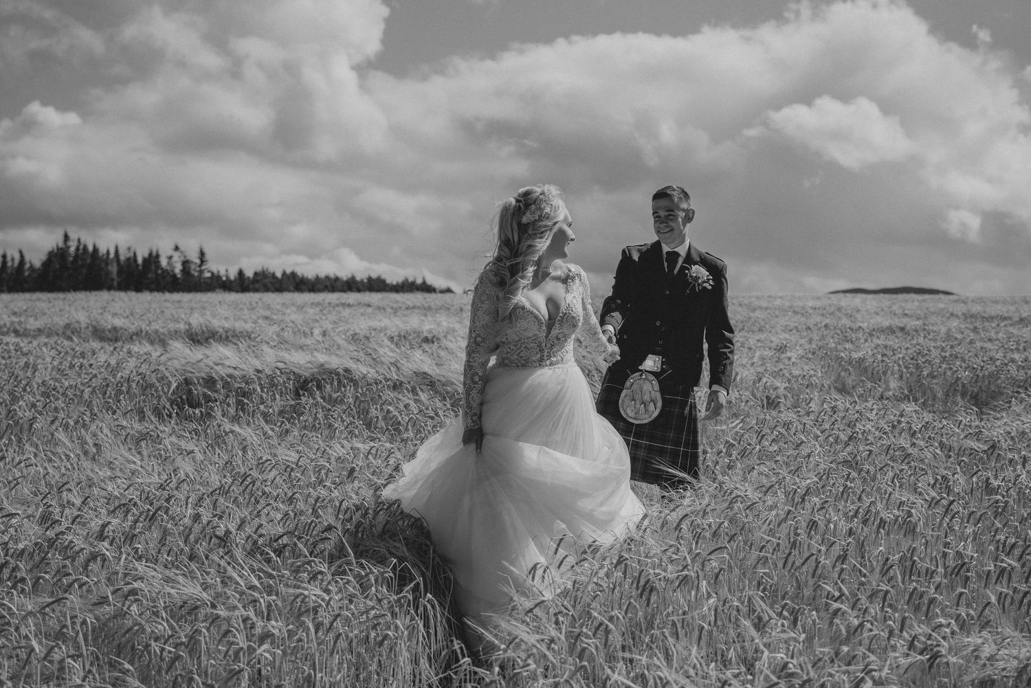 Bride and kilted groom walking through a golden wheat field in black and white.