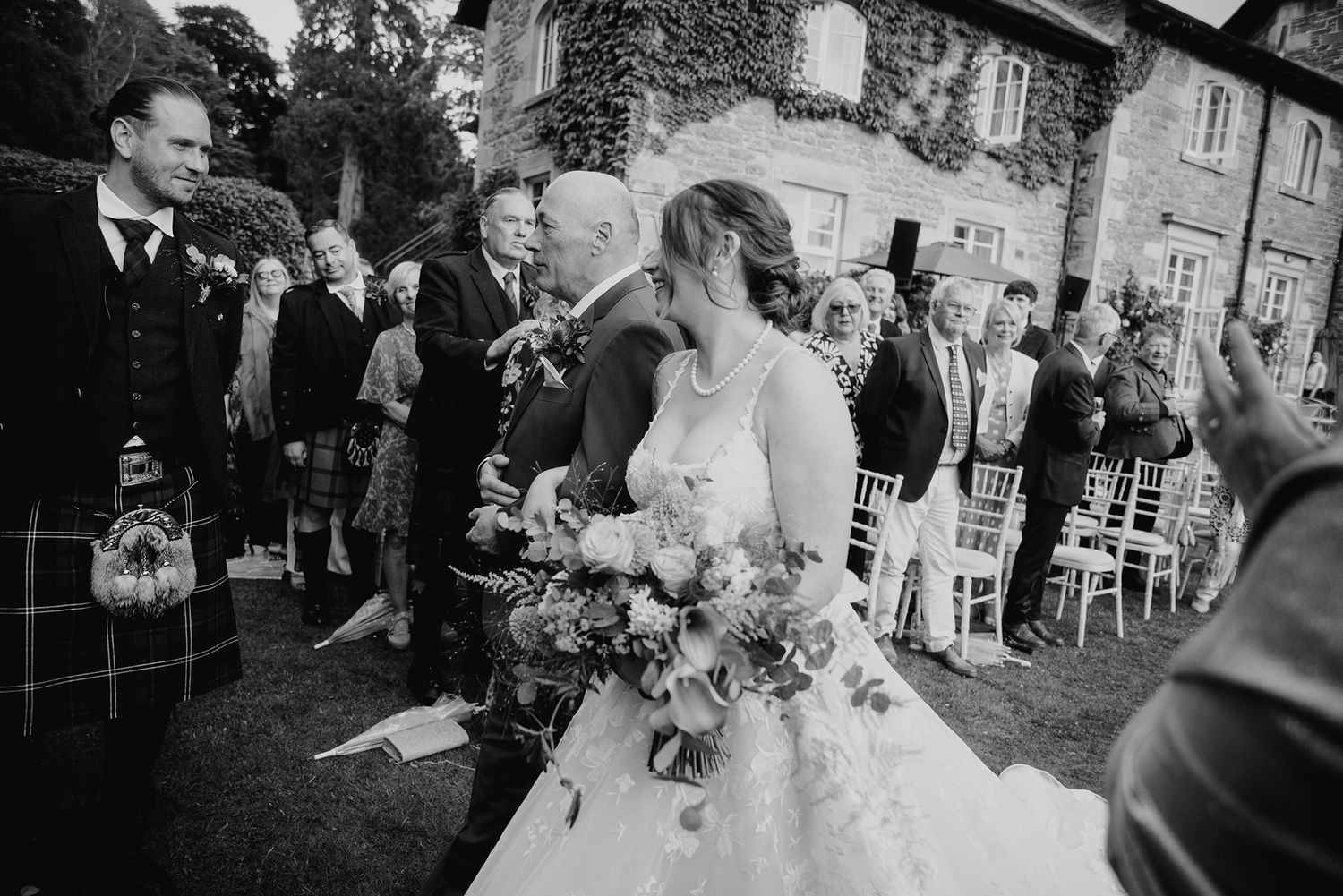 Black and white photo of bride and groom sharing first kiss at outdoor wedding ceremony.