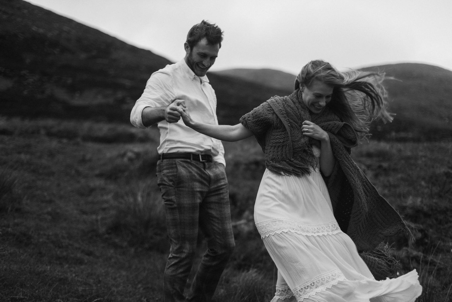 Black and white photo of couple dancing in the wind on a Scottish Highland hillside.