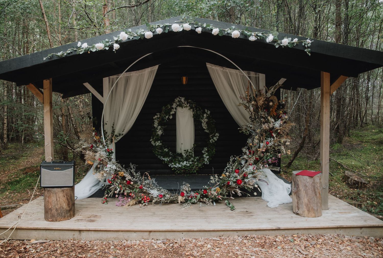 Woodland wedding ceremony arch with circular wreath, draped fabric, and lush floral arrangements.