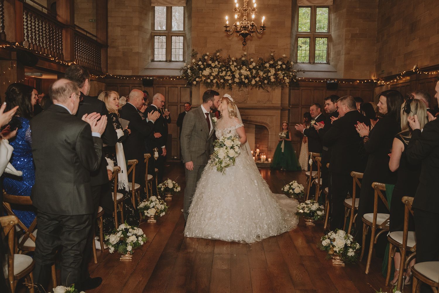 Bride and groom share first kiss at elegant indoor wedding ceremony with floral arch and candlelit venue.
