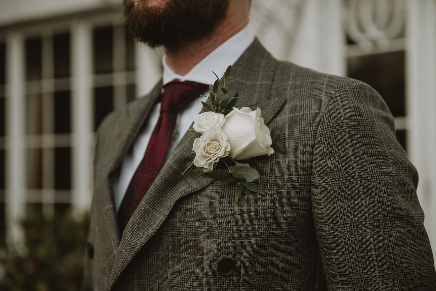 Groom in green plaid suit with white rose boutonniere and burgundy tie at wedding.