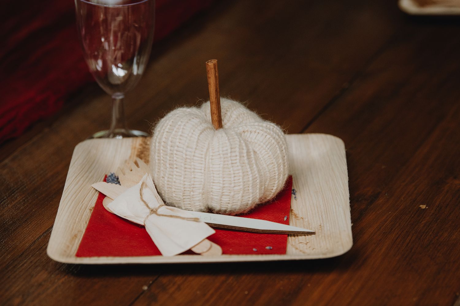 A knitted pumpkin decoration sits on a palm leaf plate with wooden cutlery at a wedding reception.