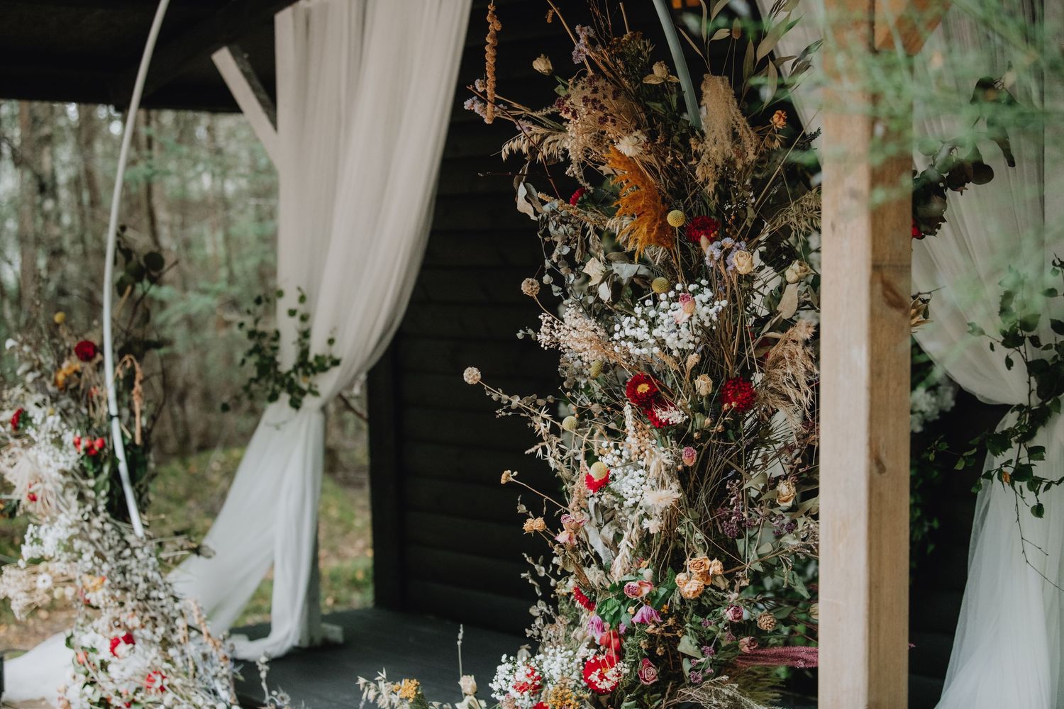 Lush dried and fresh floral arrangements decorating woodland wedding ceremony arch and pergola.