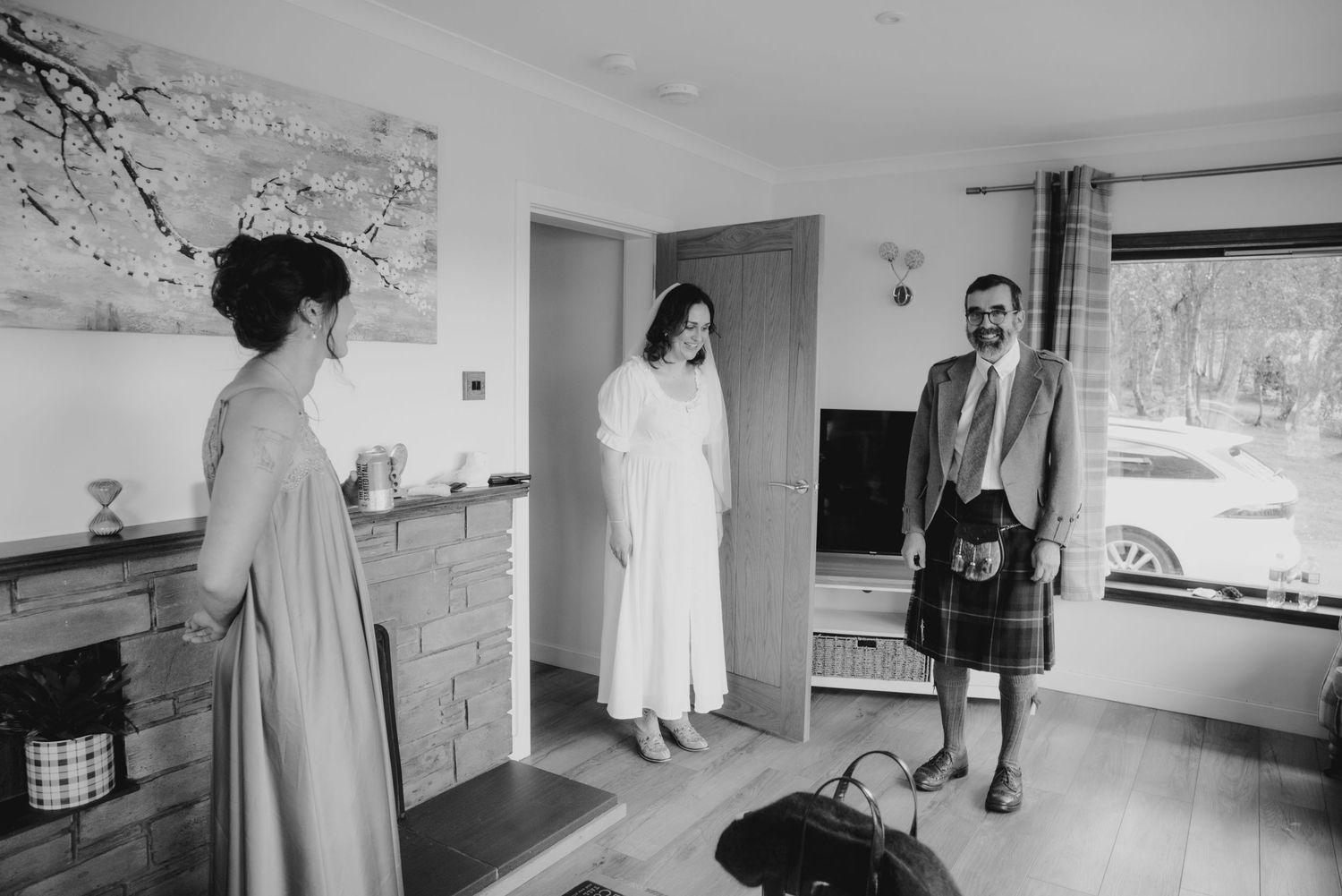 Black and white photo of bride in white dress and veil meeting groom in kilt for first look.