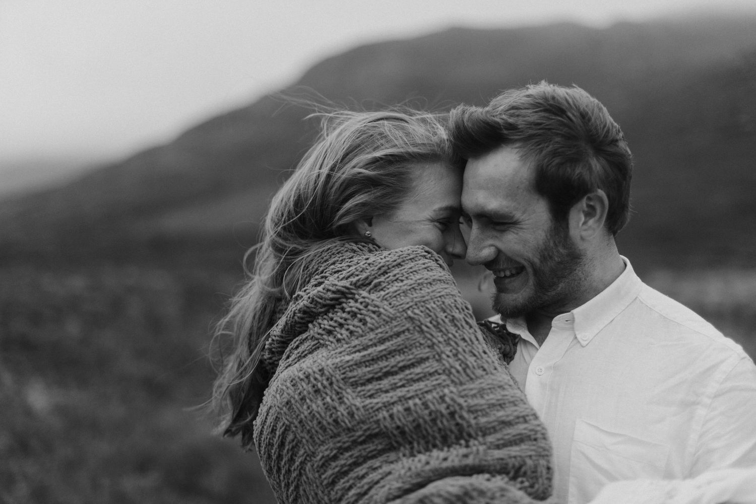 Black and white photo of a couple embracing tenderly in a misty highland landscape.