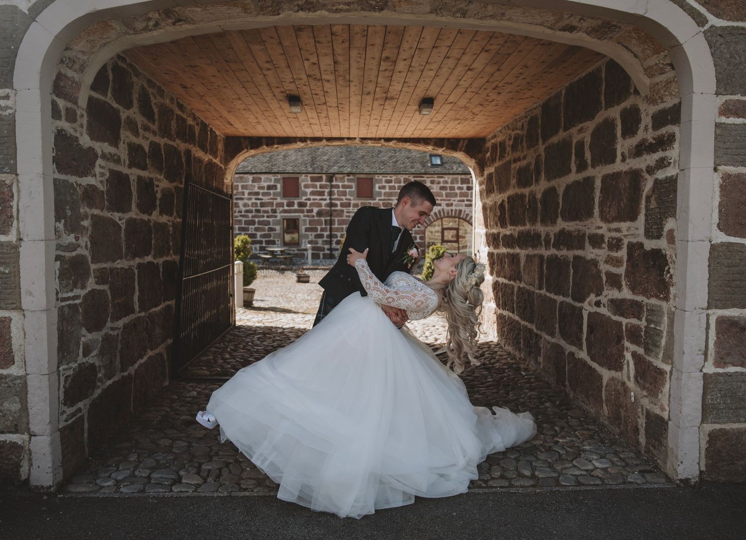 Groom dipping bride under a stone archway in a romantic wedding portrait.
