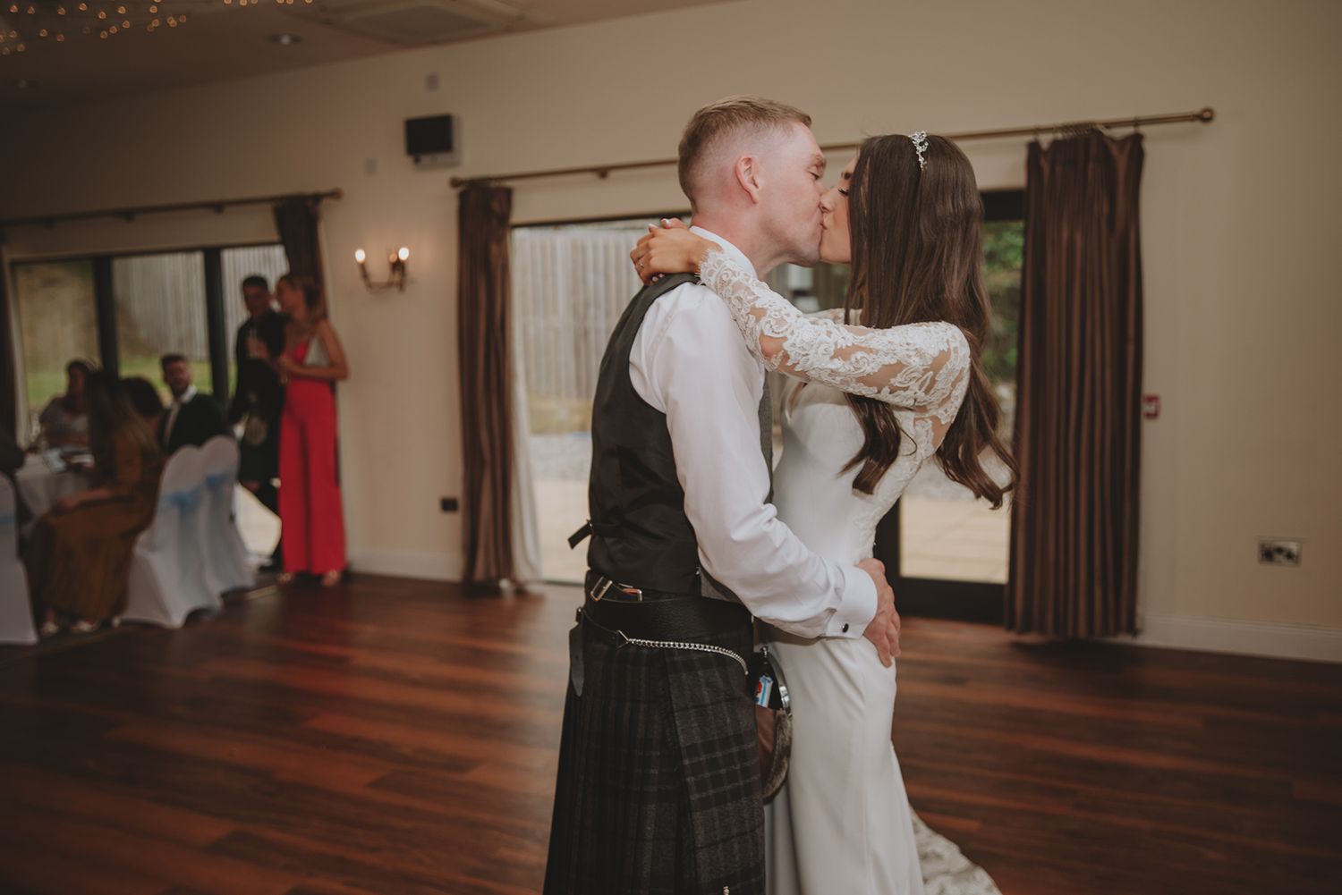Bride and groom sharing a first dance kiss, groom wearing a traditional Scottish kilt at their wedding reception.