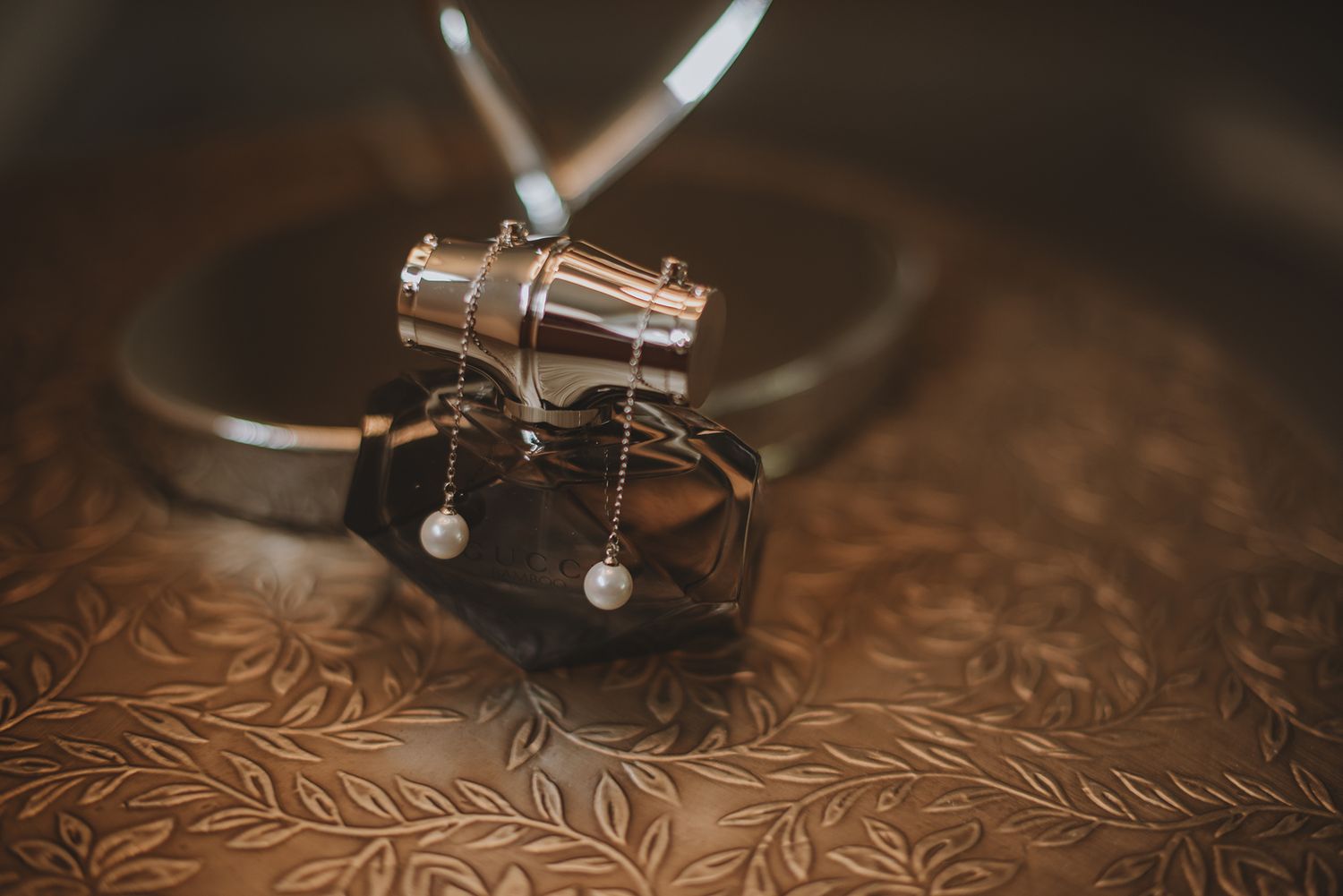 Elegant pearl drop earrings resting on a decorative bronze tray with a silver bracelet for a wedding.