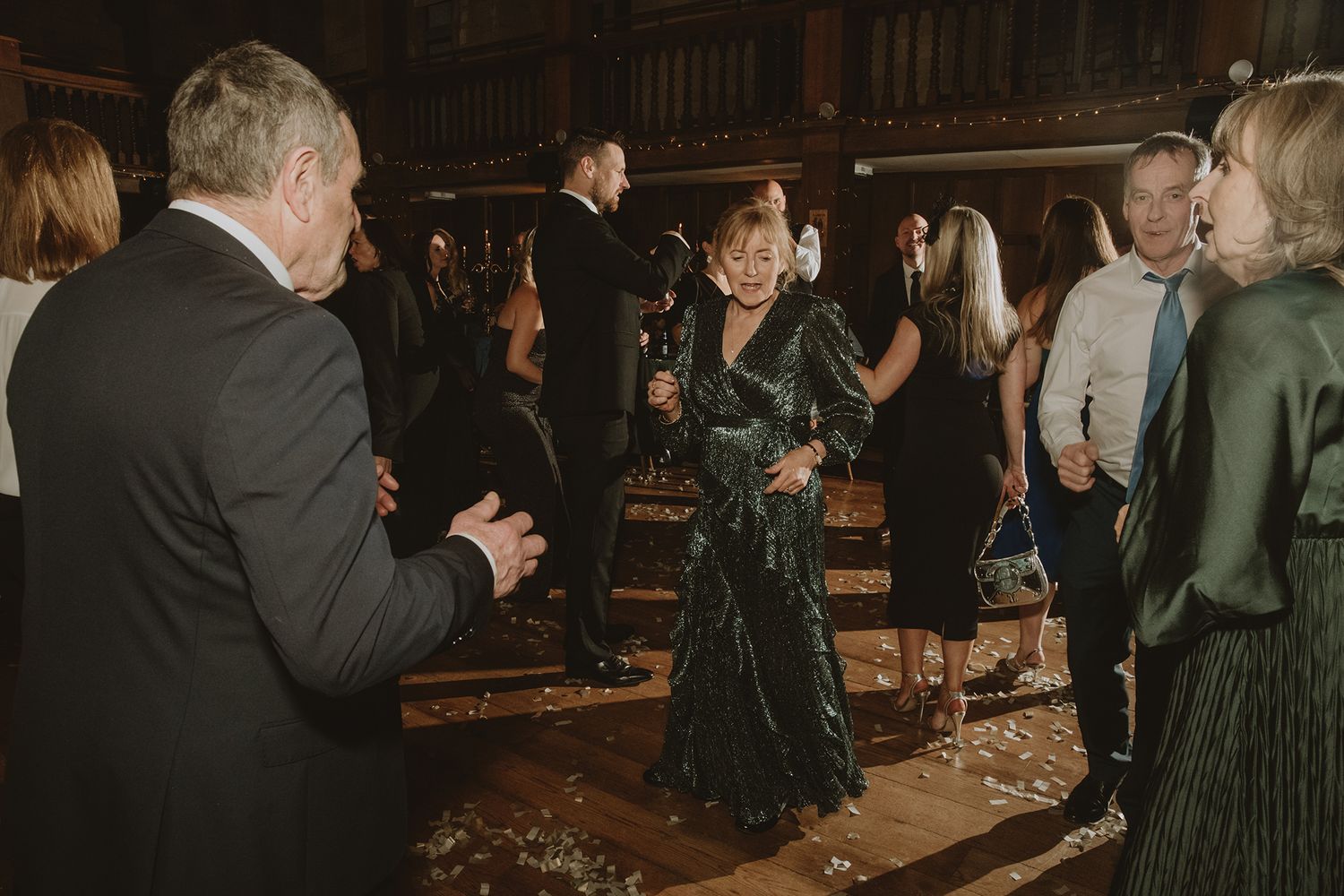 Elegant guests dancing at a formal party, woman in green sequin gown amid confetti on ballroom floor.