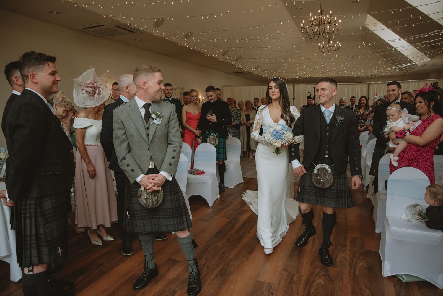 Bride and groom walk down the aisle in Scottish wedding venue, groom wearing traditional kilt, guests watching ceremony.