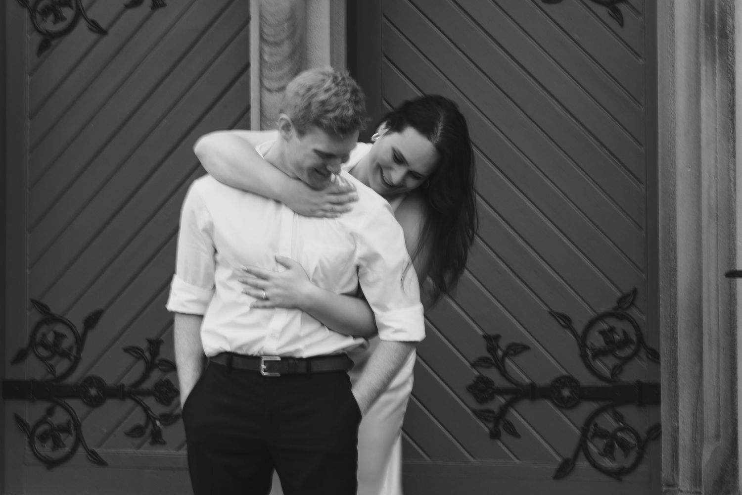 Romantic couple embracing closely in front of a dark wooden door with decorative iron details.