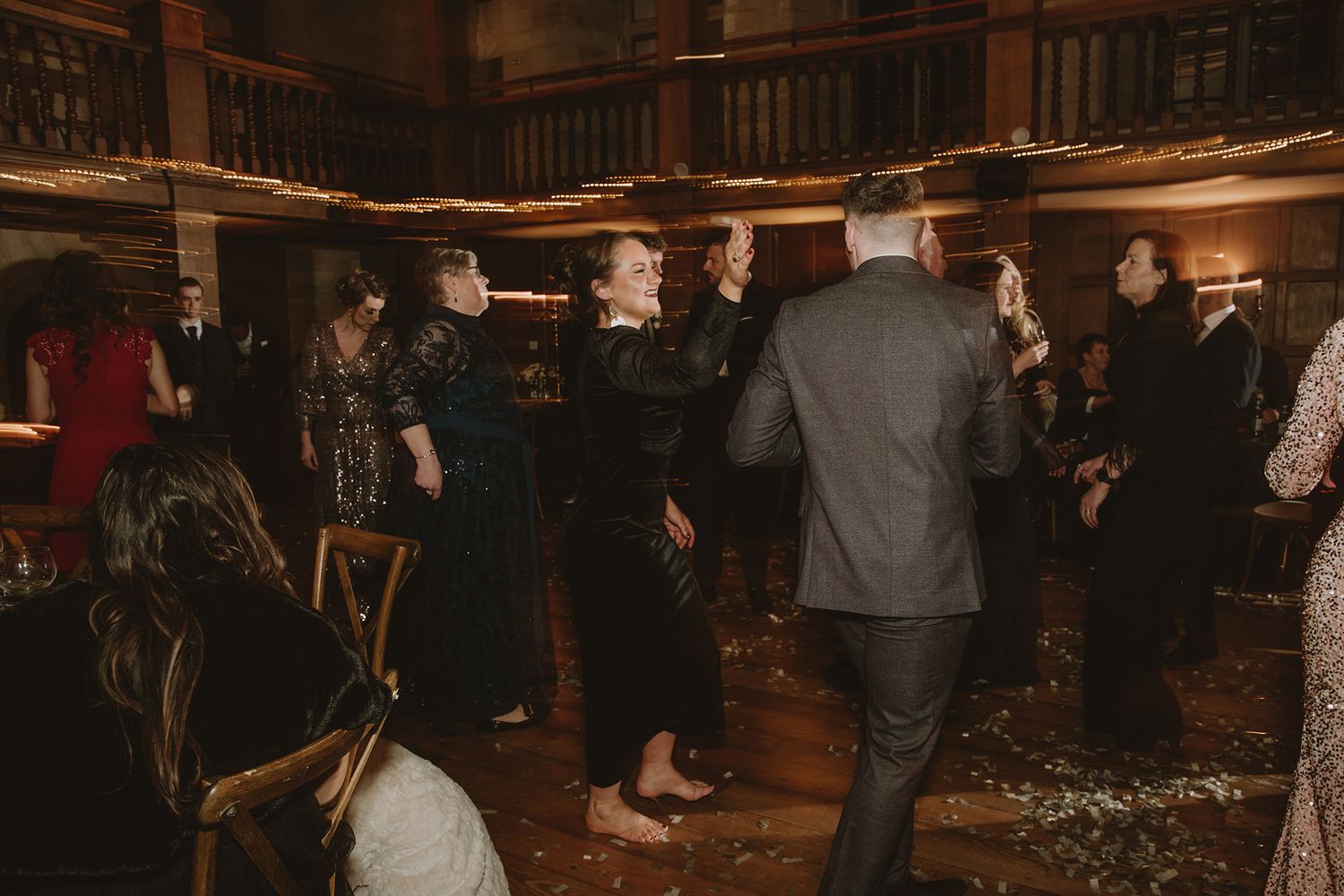 Guests dancing together on a dimly lit rustic wooden dance floor at an elegant evening wedding reception.