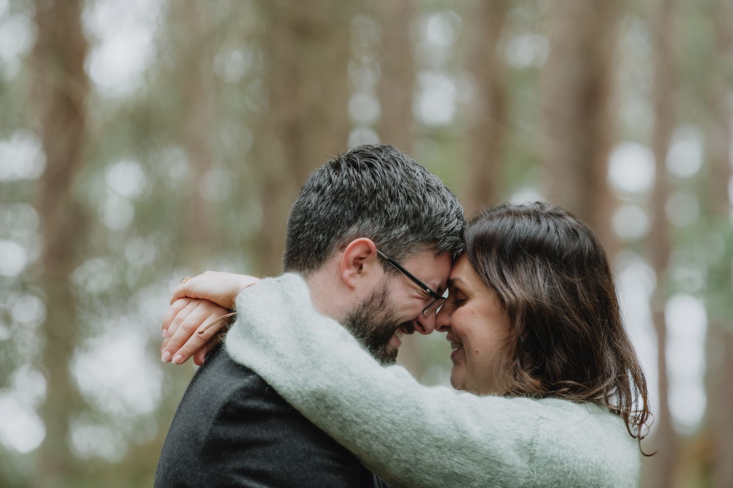 Bride and groom sharing an intimate forehead touch embrace surrounded by tall pine trees.