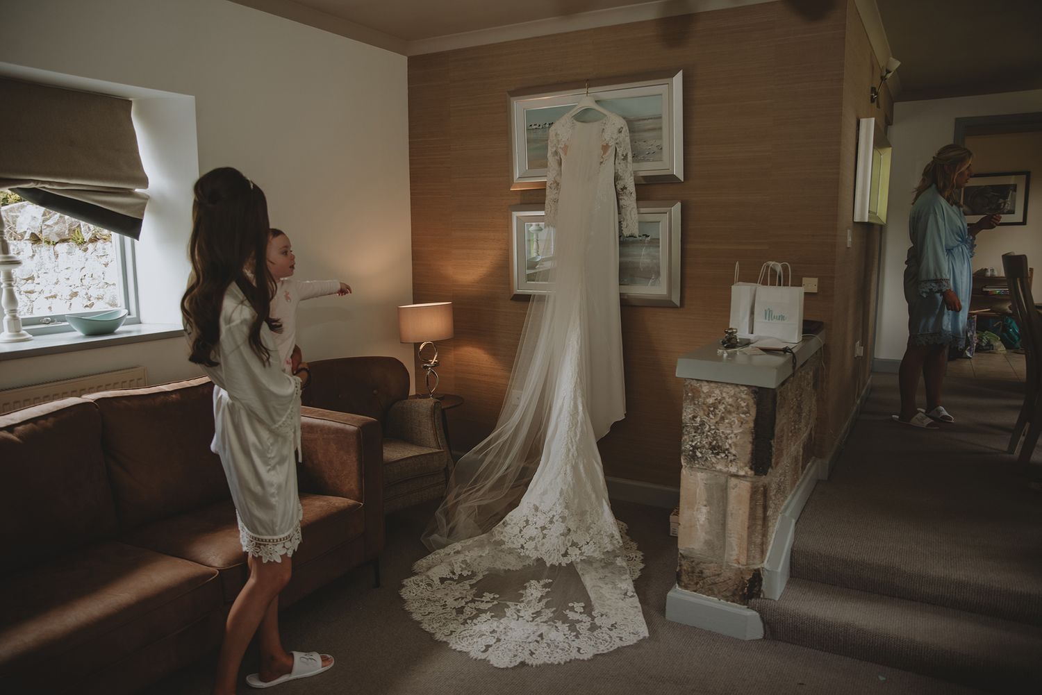 Bride admiring her elegant lace wedding dress displayed in a warmly lit hotel room before the ceremony.
